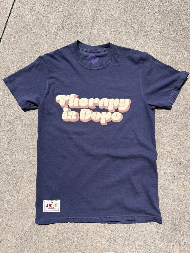 A navy blue t-shirt with the phrase "Therapy is Dope" in bold, beige letters.